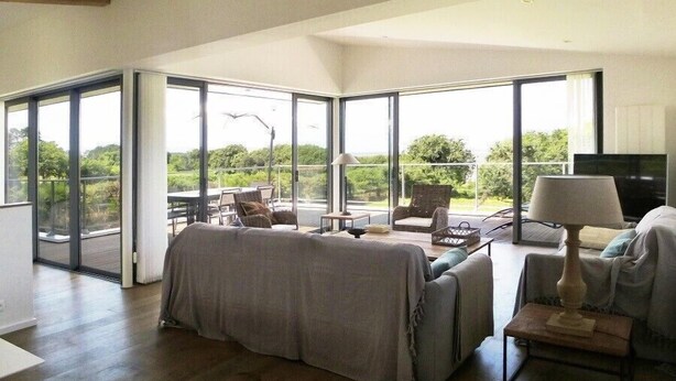 A spacious living room with a large sliding glass door leading to a balcony, a sofa, a TV, and a lamp. - Kervegan magnifique villa vue mer à Pleumeur Bodou (PLEUMEUR BODOU)