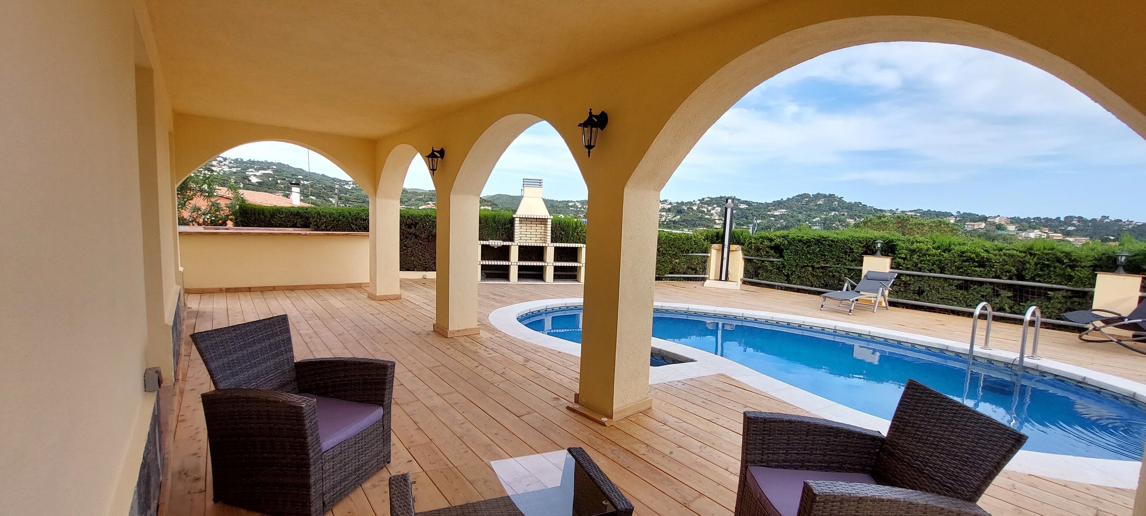 A covered outdoor area with a pool, wicker furniture, and a view of hills.