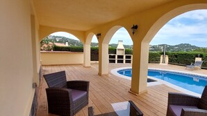 Un espacio exterior techado con piscina, mobiliario de mimbre y vistas a colinas.
