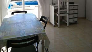 Una habitación con una mesa de comedor, sillas, un escritorio con una silla, un televisor en la pared y vista a una piscina.