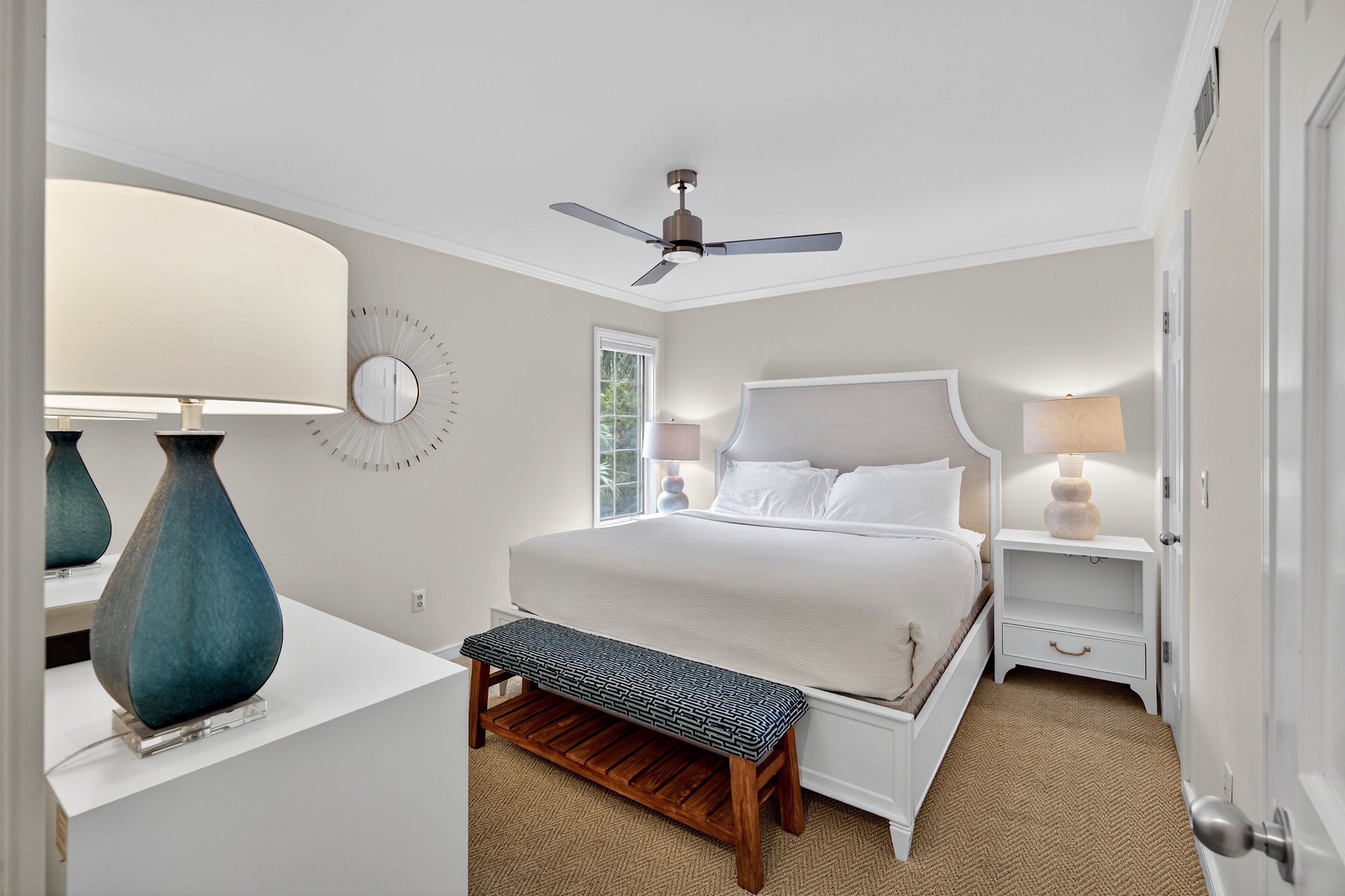 A bedroom with a bed, bedside tables, a bench, a ceiling fan, and a window.