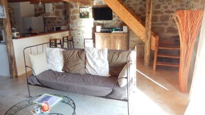 Un espacio de sala acogedor con un sofá, una mesa de centro de vidrio y una cocina al fondo.