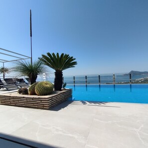 Ein Poolbereich mit Liegestühlen und Palmen, mit Blick auf einen klaren, blauen Himmel und die Ferne.