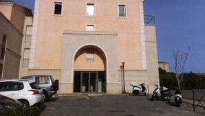 Un edificio con un arco central, varias ventanas y un estacionamiento con coches y patinetes.
