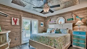 Quarto com cama, paredes de madeira, ventoinha no teto e decoração náutica.