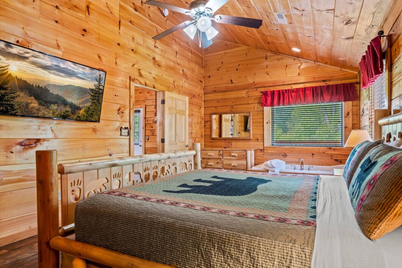 A wooden cabin bedroom with a bed, a ceiling fan, a window with blinds, and a painting on the wall.