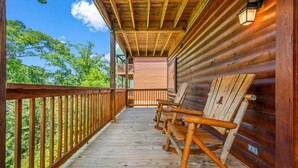 Eine Holzterrasse mit Schaukelstühlen, einem Hollergeländer und Blick auf Bäume.