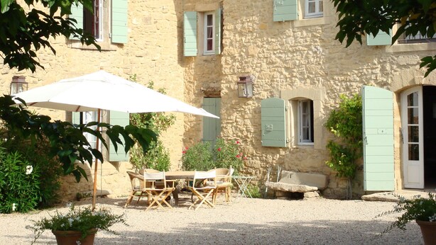 A stone building with green shutters, a table with chairs, and a white umbrella. - On 2 hectares, air-conditioned Provencal farmhouse in idyllic Provence   (L'isle-Sur-La-Sorgue)
