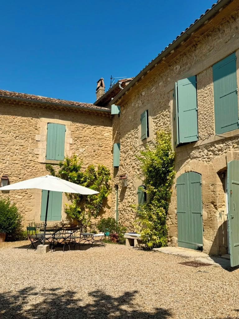 A courtyard with stone buildings, green shutters, and outdoor furniture.