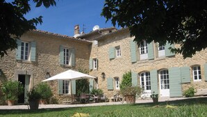 A stone building with multiple windows and shutters, a patio area with outdoor furniture, and potted plants. - On 2 hectares, air-conditioned Provencal farmhouse in idyllic Provence   (L'isle-Sur-La-Sorgue)