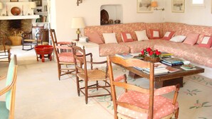 A cozy living room with a floral sofa, wooden chairs, a coffee table with books and flowers, and a fireplace. - On 2 hectares, air-conditioned Provencal farmhouse in idyllic Provence   (L'isle-Sur-La-Sorgue)