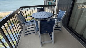 Een balkon met een ronde tafel en twee stoelen, met uitzicht op een strand.