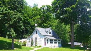 A white house with a gabled roof, surrounded by lush green trees and a well-maintained lawn.
