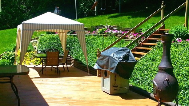 A wooden deck with a covered seating area, a birdhouse, and a decorative metal pot.
