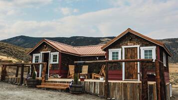 A rustic wooden house with a red exterior and a metal roof, featuring a porch with wooden chairs and a small table.