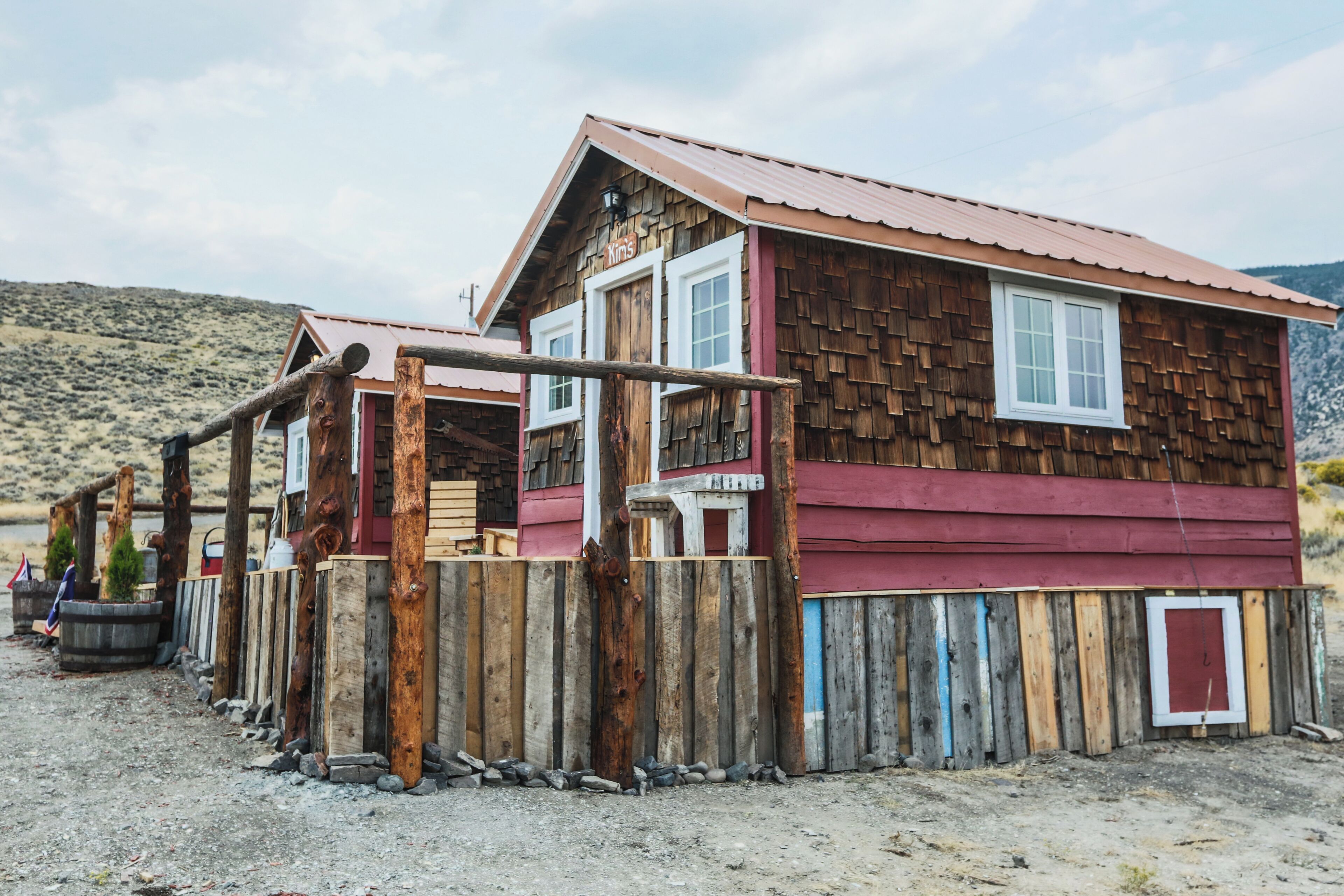 A rustic wooden building with a red roof, a wooden fence, and a mountainous backdrop.