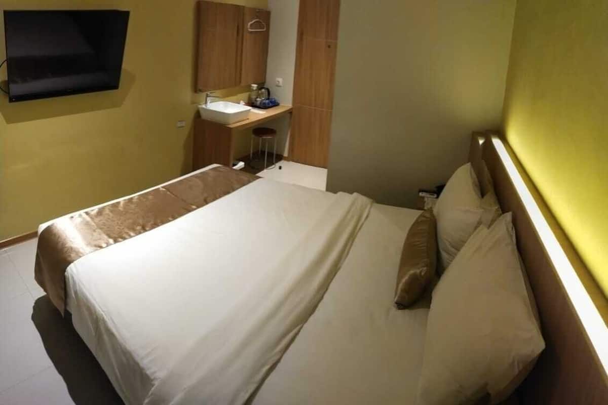 A hotel room with a bed, a desk with a chair, a sink, and a television mounted on the wall.