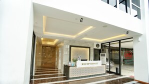 A reception desk with a sign reading "RECEPTIONIST" in a modern lobby with a marble floor and glass doors leading outside. - Deli Hotel (Medan)