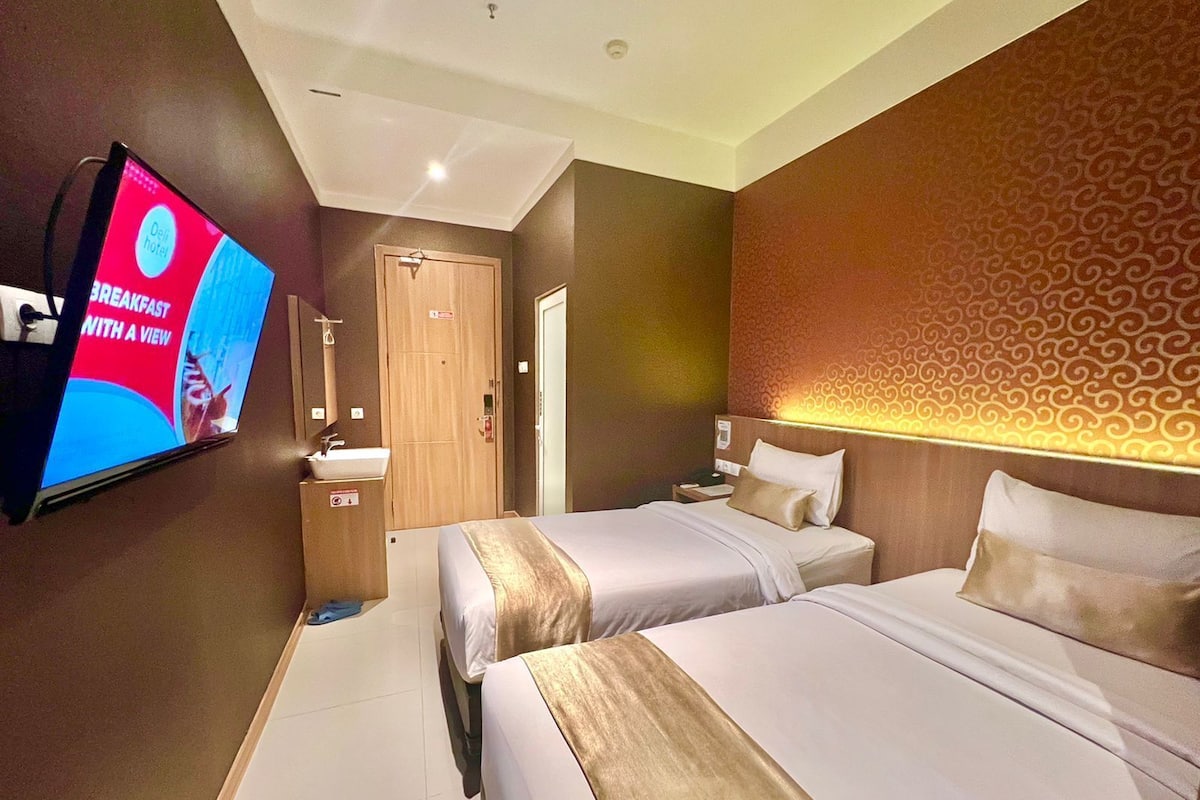 A hotel room with two beds, a TV mounted on the wall, a bathroom, and a patterned wall.