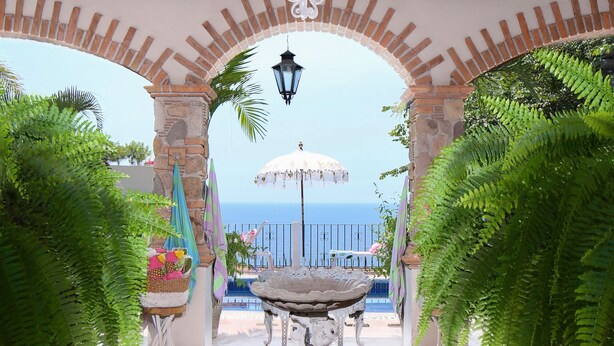 An outdoor patio with a wrought iron chandelier, stone arches, and a view of the sea.
