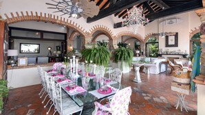 A dining area with a glass table, white chairs, and a brick floor.