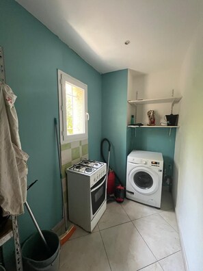Un lavadero pequeño con estufa a gas, lavadora y ventana.