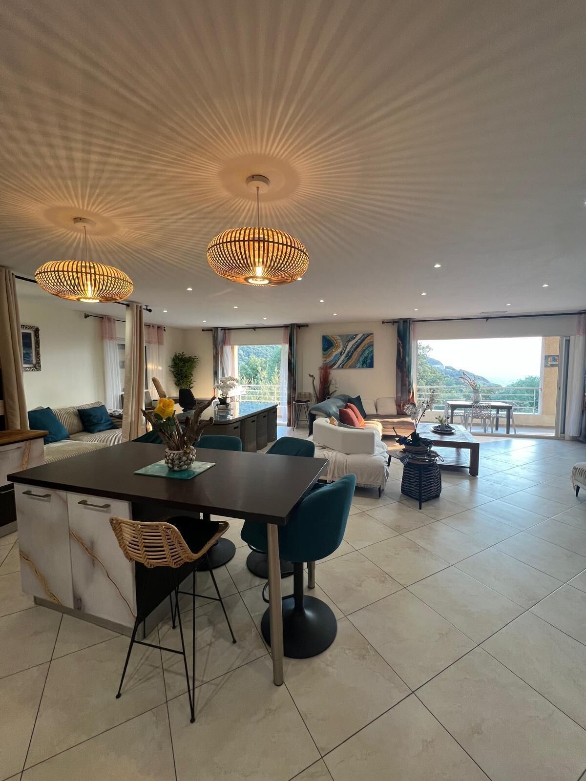 A spacious living area with a dining table, chairs, and a sofa. There is a large window providing a view of the outdoors.