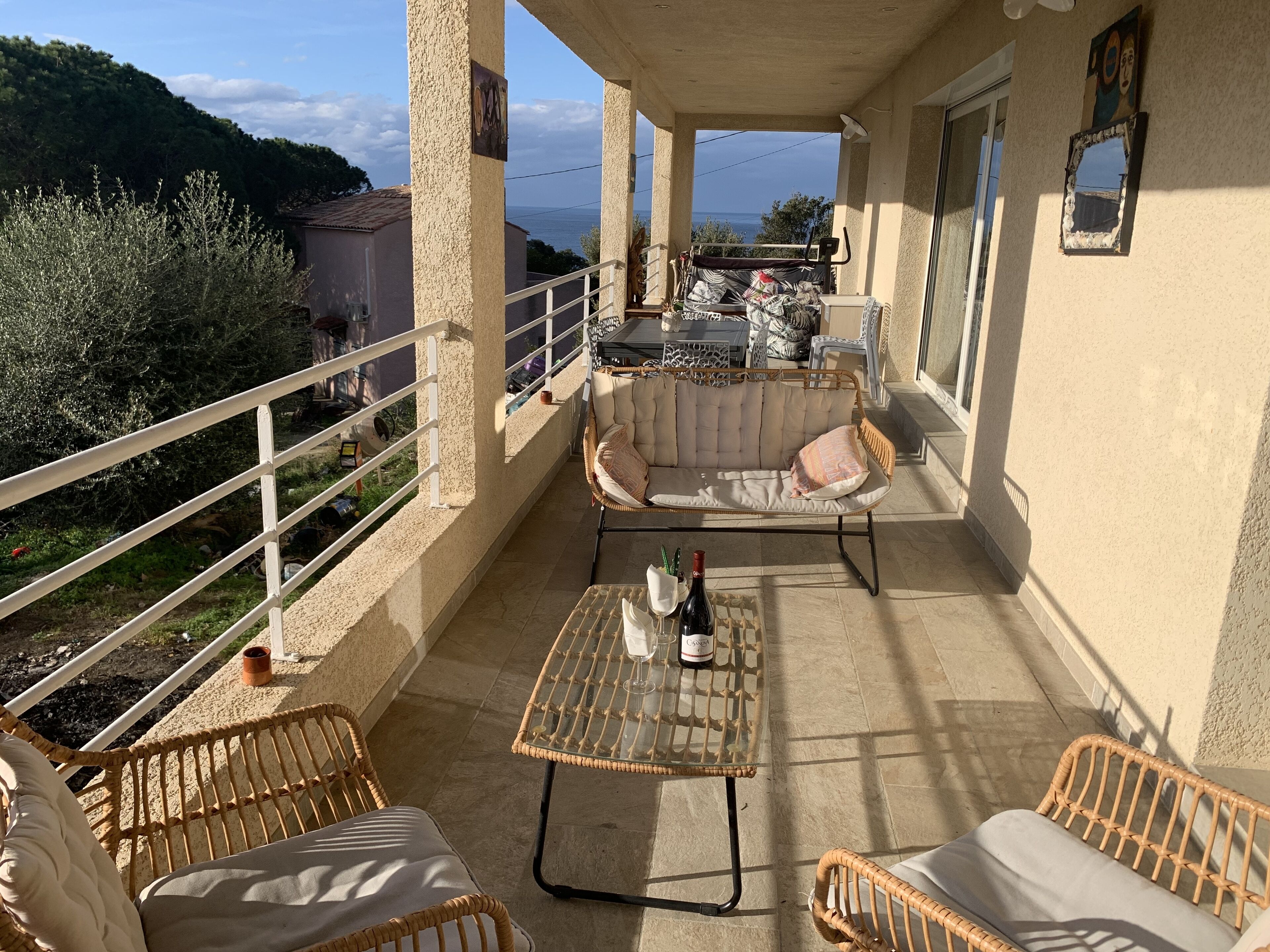 Een balkon met rieten meubels, een tafel met een fles en een bank.