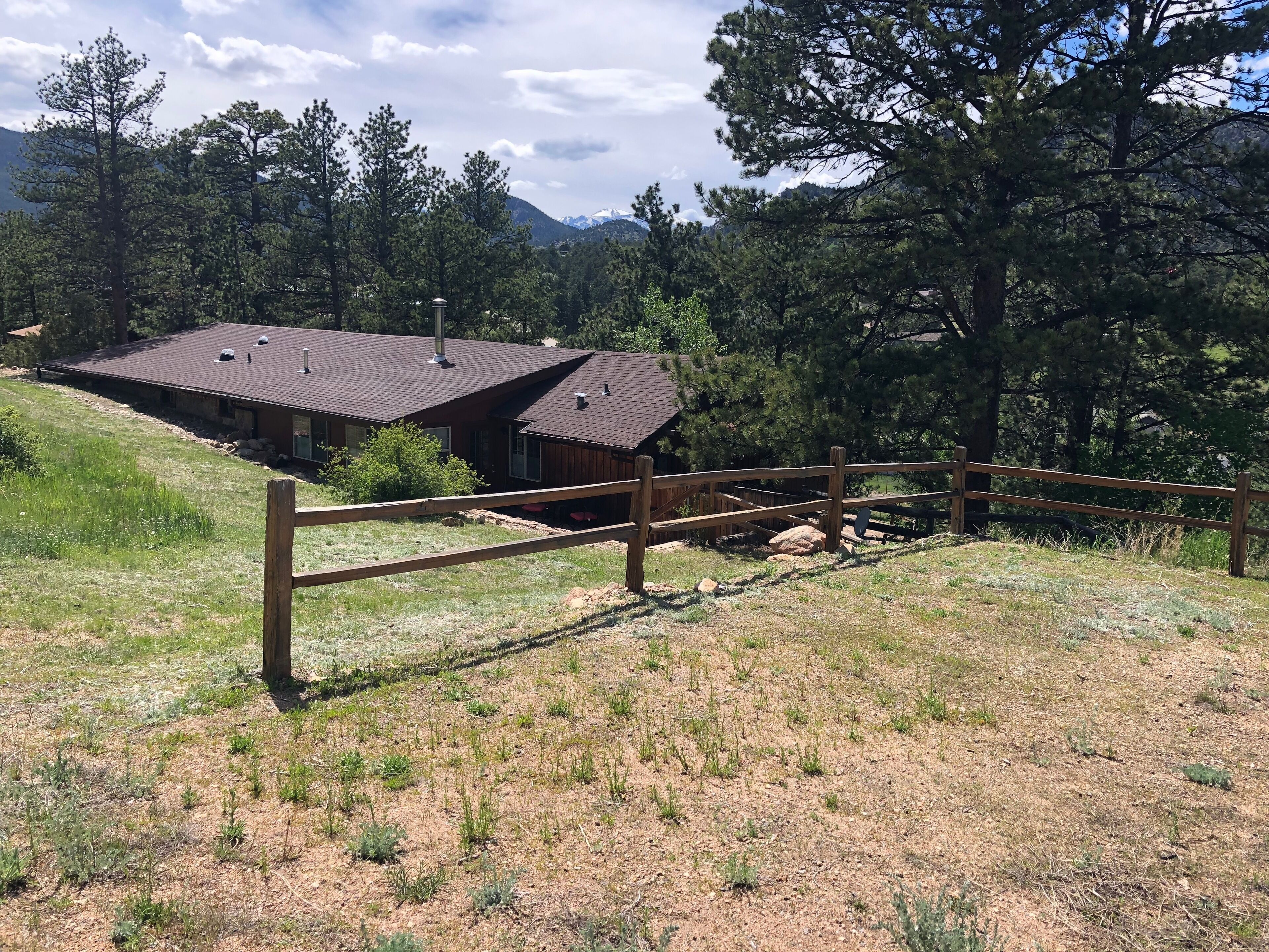 A rustic cabin with a sloped roof, surrounded by a wooden fence and a grassy area.