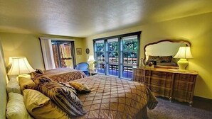 A bedroom with a large bed, a dresser, and a chair. There is a window with a view of trees.