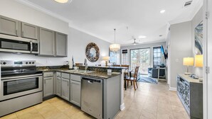 A modern kitchen with stainless steel appliances, a granite countertop, and a dining area with a chandelier.