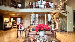 Un'ampia zona giorno con soffitto alto, una grande scultura a forma di albero, un accogliente camino e una decorazione con la scritta 'Merry Christmas' su un tavolino.