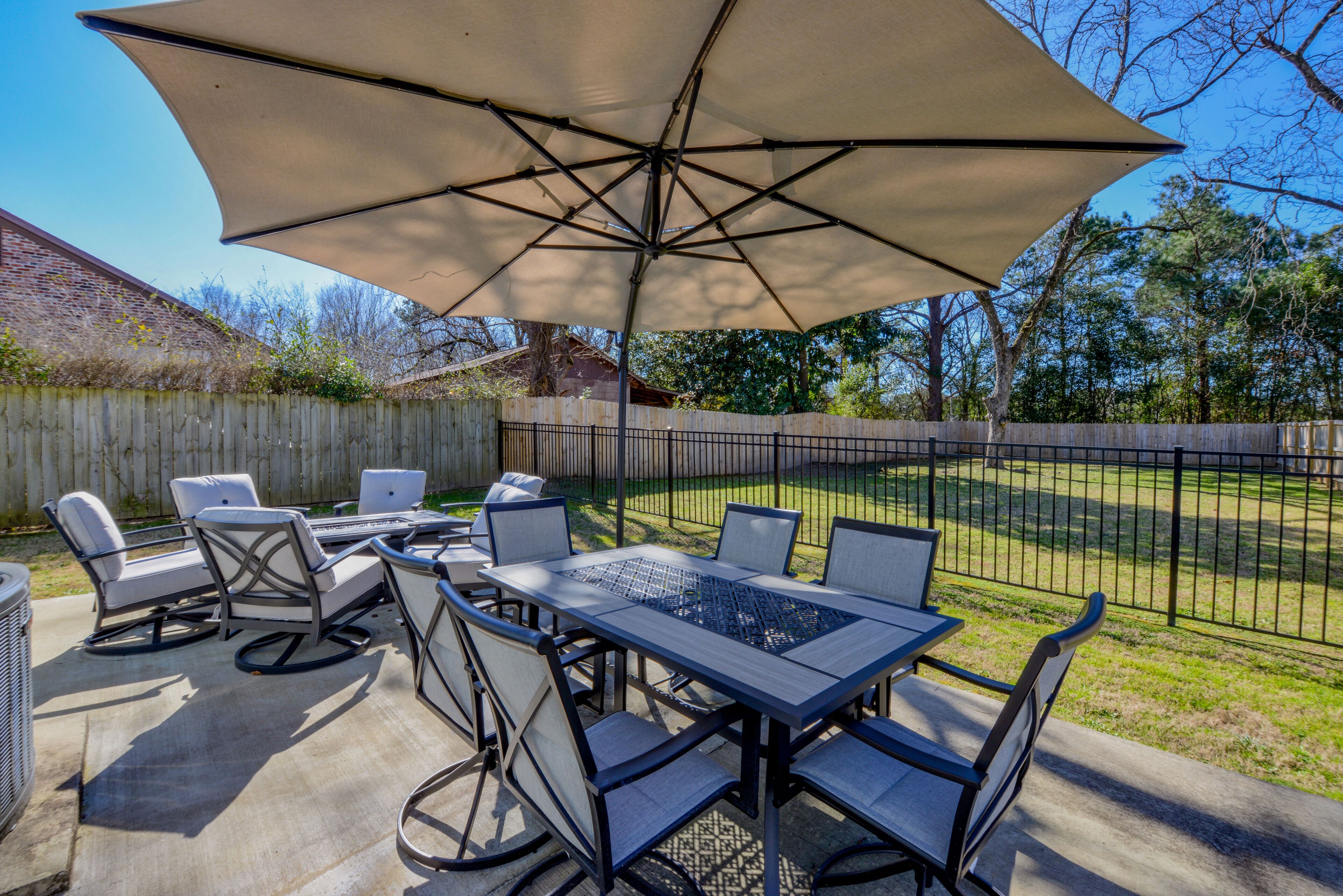 An outdoor patio with a table and chairs, a large umbrella, and a wooden fence in the background.