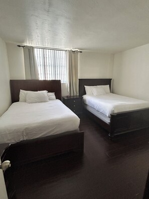 A hotel room with two single beds, a nightstand, a window with curtains, and a wooden floor. - Beachfront Property, Ocean Views! (Hollywood)