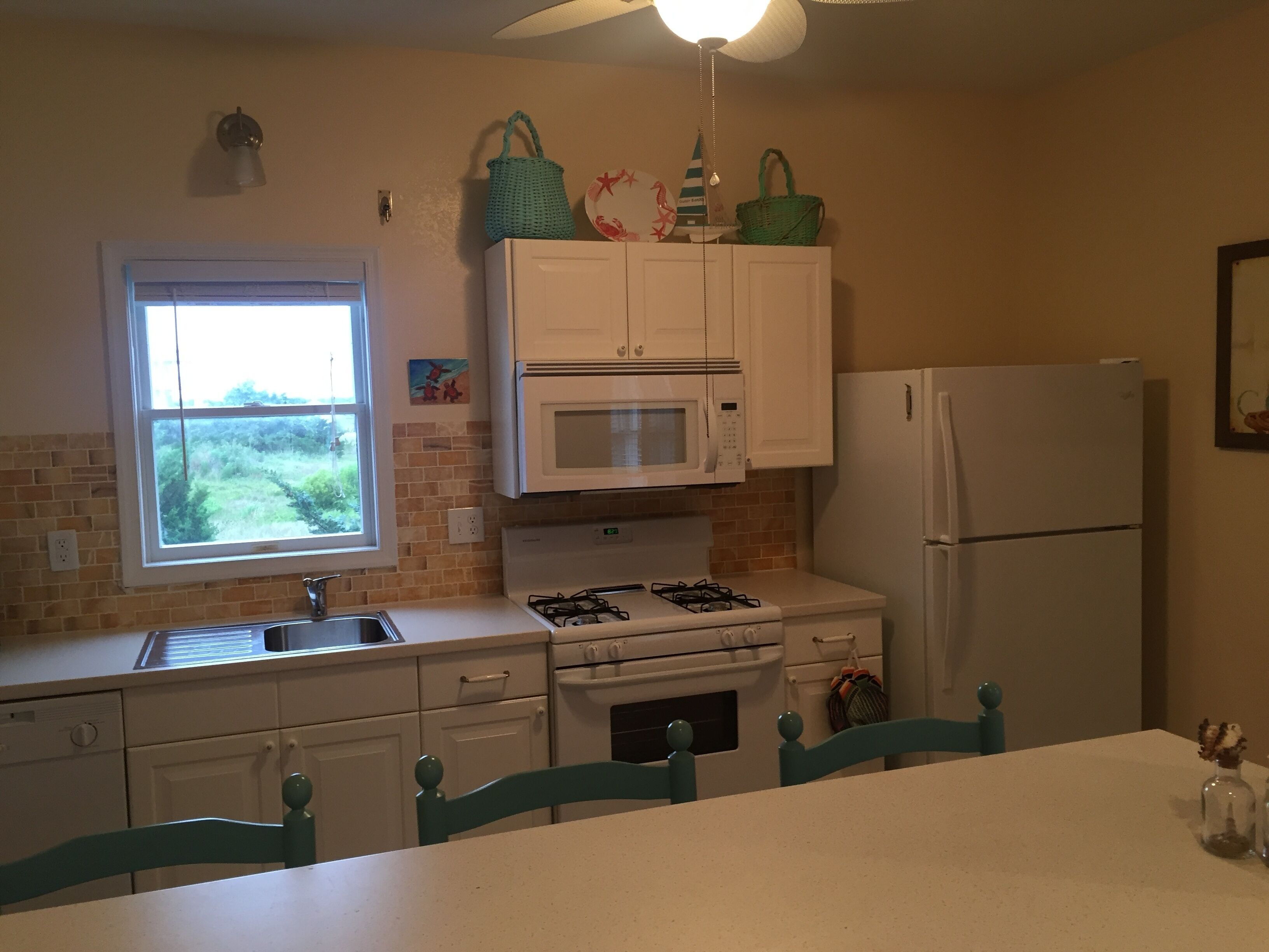 A kitchen with white cabinets, a microwave, a gas stove, a refrigerator, and a window with a view of greenery.