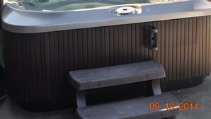 Ein Whirlpool mit Sitzbank, umgeben von einem Holenzaun, mit einem Haus im Hintergrund.