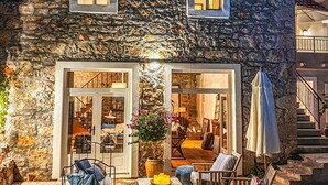 Una casa de piedra con balcón, un comedor con mobiliario exterior y una escalera que lleva a un nivel superior.