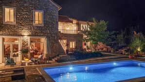 Una casa de piedra con piscina, mobiliario de exterior y una escalera que lleva a un segundo piso.