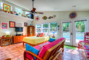 A spacious room with a bed, a desk, and a TV. There are windows and a door leading outside.