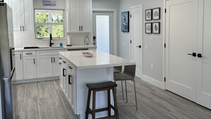Une cuisine moderne avec des meubles blancs, un grand îlot central et une vue sur l’extérieur.