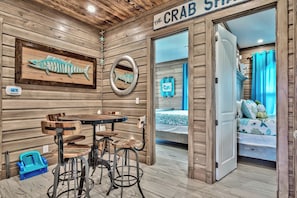 Experience the nautical charm of The Crab Shack, featuring a round table, metal stools, and a cozy cabin-like atmosphere.