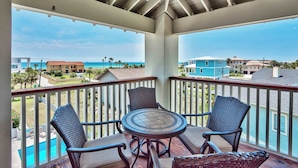 A balcony with wicker furniture, a view of the ocean, and a pool.