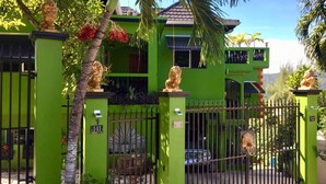 A green house with a gated entrance, lion statues on the pillars, and a number 141 sign. - GD Rooftop Lounge ocean view, salt water pool with mountain view, 1bdrm (West Gate Hills, Montego Bay)