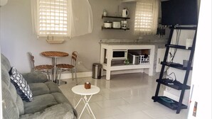 A living room with a gray sofa, two wooden chairs, a small white table, and a TV on a black stand. - GD Rooftop Lounge ocean view, salt water pool with mountain view, 1bdrm (West Gate Hills, Montego Bay)