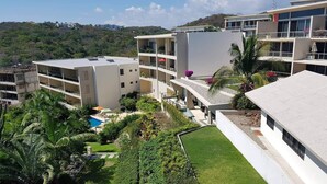 Un hotel de varios pisos con piscina en la azotea, rodeado de abundante vegetación y un paisaje montañoso.