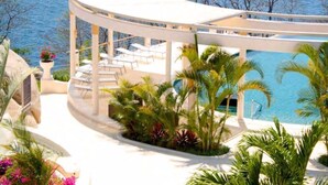 Un espacio exterior circular con piscina, rodeado de palmeras y vista al mar.