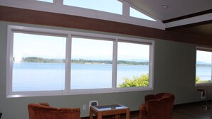 A room with large windows overlooking a lake, wicker chairs, a small table, and wooden beams on the ceiling.