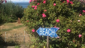 A sign pointing to the beach, surrounded by lush greenery and pink flowers.