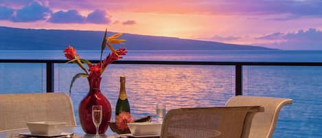 A table set for dining with a view of the sea and a sunset.