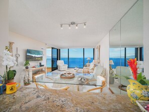 Ein geräumiger Wohnbereich mit einem Glastisch, bequemen Sitzmöglichkeiten, einem Flachbildfernseher und Blick aufs Meer.